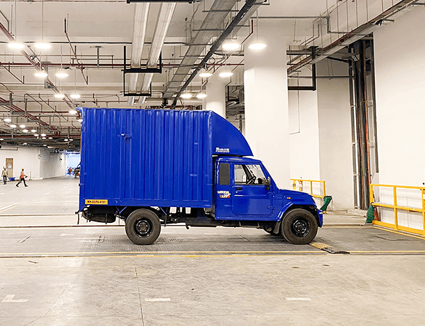 A blue pickup truck with a covered cargo area is parked in a warehouse