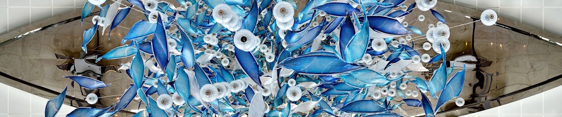 A large, intricate glass sculpture with blue and white elements hangs from a ceiling.